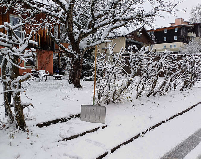 Ein Schneeschieber mit silberner Schaufel steht an einem verschneiten Gehweg