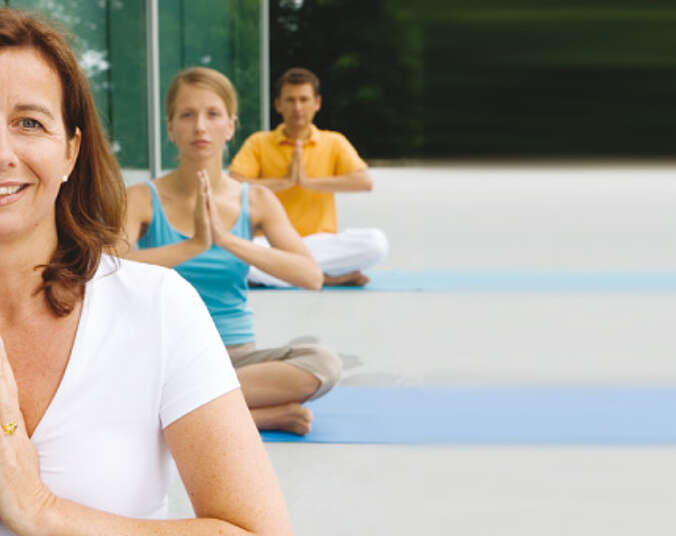 Zwei Frauen und ein Mann sitzen im Schneidersitz beim Yoga.
