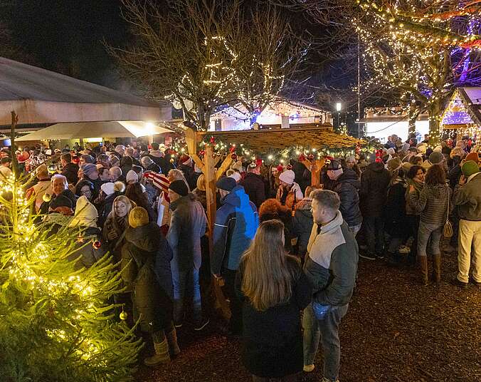 Frauen und Männer stehen im weihnachtlich beleuchteten Winterdorf im Lammgarten an Stehtischen.