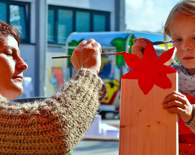 Eine Frau und ein Mädchen bemalen ein Holzbrett.