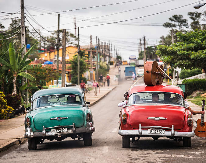 Zwei alte Cadillacs. einer türkis, einer rot, stehen auf einer Straße nebeneinander.