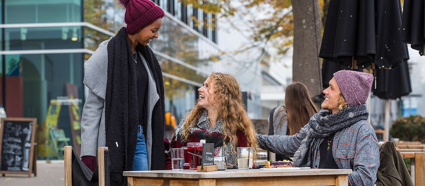 Junge Leute sitzen in Straßencafe warm eingepackt